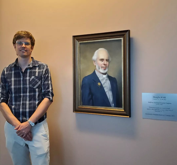 a painting of a friendly looking man. the artist stands next to the portrait.